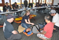 Students observe as Dean Charles is strapped onto a clamshell. From left, instructor Justin Beaumont, Candace WInter and trainees Aaron Watts and Hank Gus.
