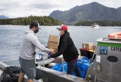Jason Cole (left), Power To Be's chief strategy officer, hands Tory Atleo Sr. supplies flown in by the non-profit organization onto the Ahousaht Lone Cone crew boat in Tofino.