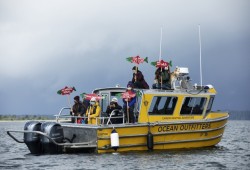 Protestors aboard an Ocean Outfitters' boat hold up signs that read, "protect what you love," and "swimming toward extinction," during a wild salmon flotilla in the Tofino harbour.