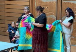 Sayers’ mom Judith and Aunt Brenda wrap her in a blanket at a joyful dissertation defense at the University of Victoria First Peoples House, Ceremonial Hall.