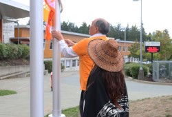 Jeff Cook and Saryta Dick raise Survivor’s flag in front of the Alberni District Secondary School.