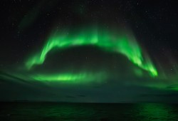 The green Northern Lights, or Aurora Borealis, are seen above the ocean. (Tolstnev photo)