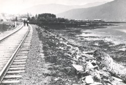 Two figures walk down the railway tracks in 1917, next to where the Somass sawmill would be built 18 years later. In the distance is the growing townsite of Port Alberni. To the north was the location of ƛuukʷatquuʔis, a Tseshaht winter village site. (Joseph Clegg/Alberni Valley Museum Photograph Collection PN00162)