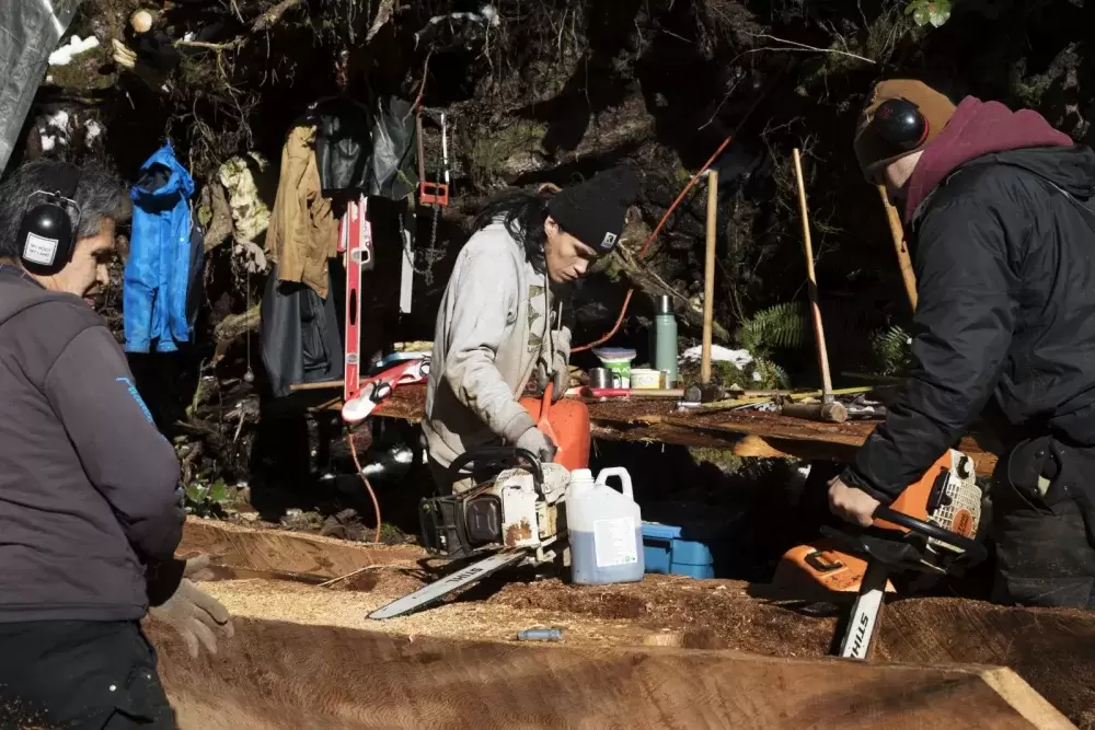 Ryan Sabbas (centre) and Joshua Watts (right) help Joe Martin carve a canoe for Valeen Jules within Tla-o-qui-aht First Nation traditional territory off of the Pacific Rim Highway, on Feb. 16, 2021. 