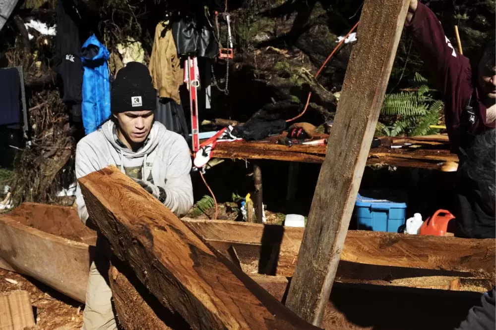 Ryan Sabbas (left) and Joshua Watts lift a piece of cedar that was carved from the hull of a dugout canoe within Tla-o-qui-aht First Nation traditional territory off of the Pacific Rim Highway, on Feb. 16, 2021. 