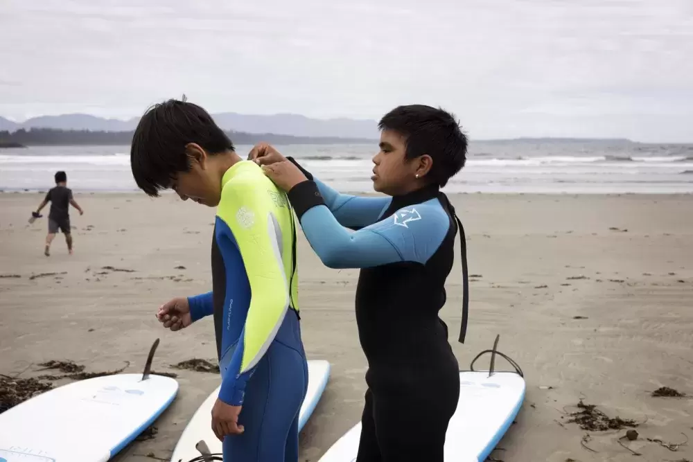 Payton Williams (right) helps Nathan Atleo zip up his wet suit in front of Esowista, near Tofino, on June 14, 2021.