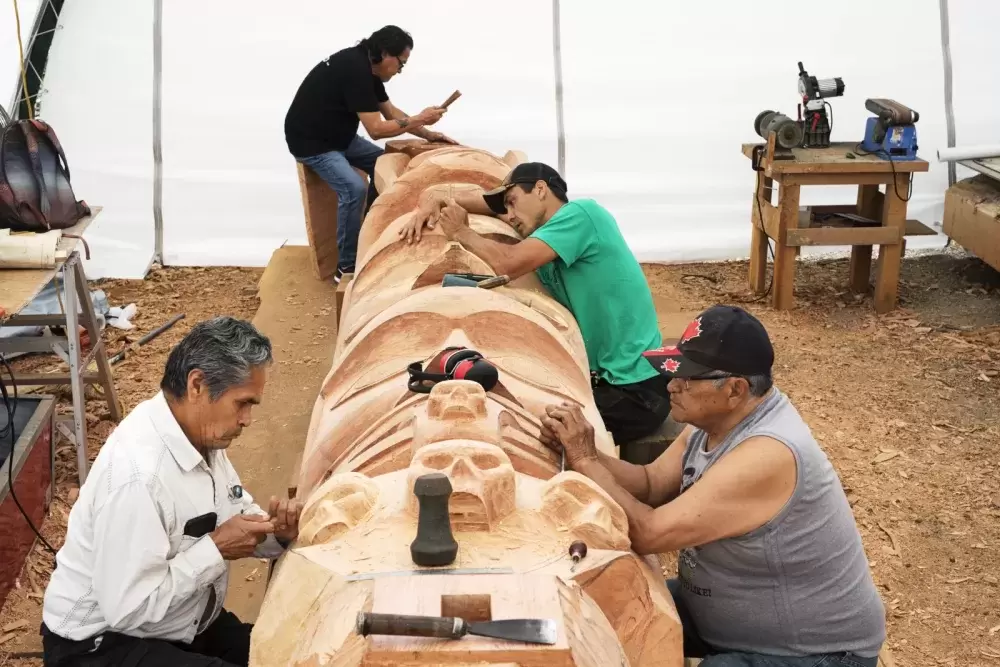 (From left to right) Joe Martin, Patrick Amos, Robin Rorick and Robert Martin (Nookmis) carve a totem pole inside a tent set up at the Tofino Botanical Gardens, on July 9, 2021.
