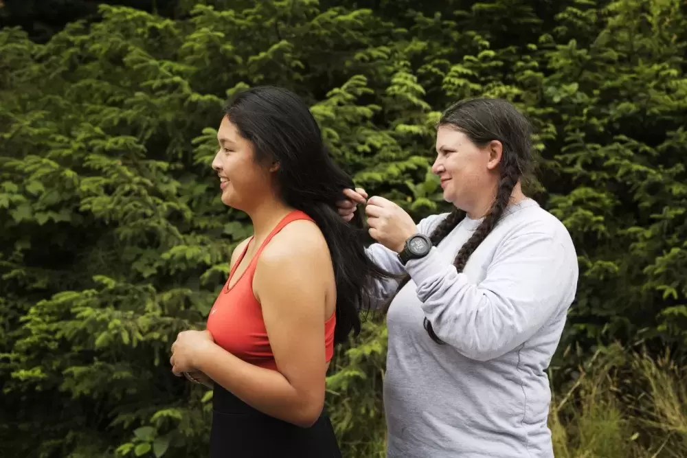 Tseshaht First Nation warrior youth coordinator Randi-leigh MacNutt, braids Brandi Lucas' hair before she slips her wetsuit overhead, in Ucluelet, on August 18, 2021.