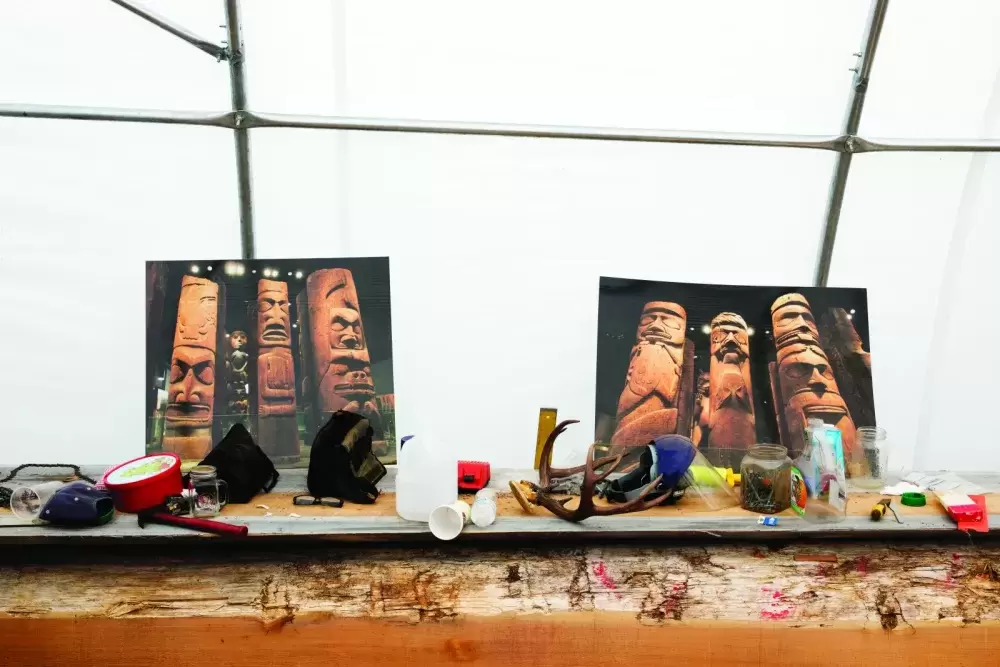 Pictures of Nuu-chah-nulth totem poles sit on a work to serve as a visual reference for a totem pole that is being carved at the Tofino Botanical Gardens in Tofino, on July 7, 2021.