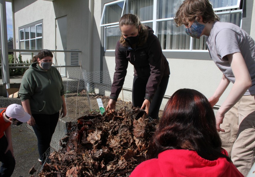 Gabriella Stanley (centre) Gracie Martinez (left), Julian Larrivee-Woods and other students in the Grade 8-9 class move leaves that have been composting by the Eighth Avenue Learning Centre over the winter.